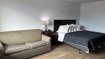 Et hotelværelse med en seng, et natbord, en lampe og en sofa.