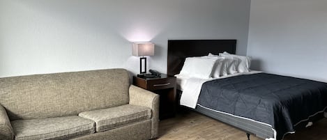 Une chambre d’hôtel avec un lit, une table de chevet, une lampe et un canapé.