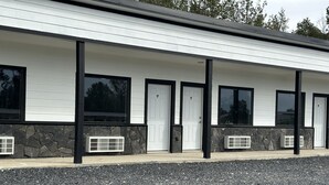 A modern building with a white exterior, black trim, and stone accents. It features multiple doors and windows, with a gravel driveway in front. - Hochabel Hotel (Idabel)