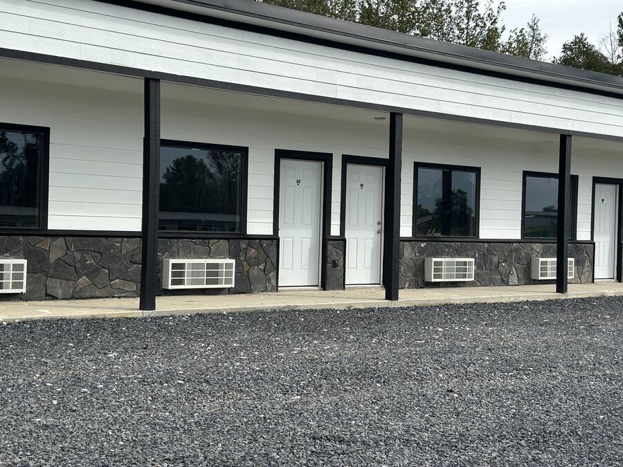 A modern building with a white exterior, black trim, and stone accents. It features multiple doors and windows, with a gravel driveway in front.