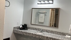A bathroom with a granite countertop, a sink, a mirror, and a towel rack. - Hochabel Hotel (Idabel)