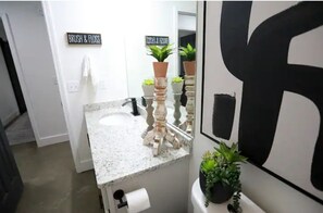 A bathroom with a white sink, a mirror, and a towel rack. There are two potted plants on the counter. - SunChaser 042 (Brandon)