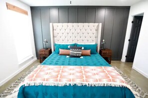 A bedroom with a tufted headboard, a teal bedspread, and two bedside tables with lamps. - SunChaser 042 (Brandon)