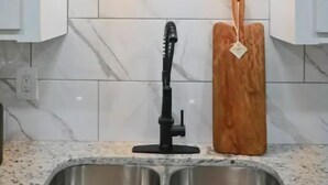 Una cocina con un lavamanos doble de acero inoxidable, un grifo negro y una tabla de cortar de madera con una etiqueta.