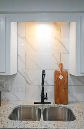 Una cucina con un lavello in acciaio inossidabile a due vasche, un rubinetto nero e un tagliere di legno con un'etichetta.