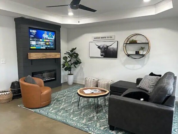 A modern living room with a flat-screen TV, a fireplace, a sofa, a coffee table, and a decorative plant. - SunChaser 042 (Brandon)
