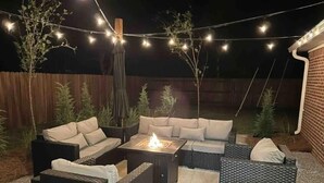 Un patio al aire libre con un conjunto de sofás, un brasero y luces colgantes.