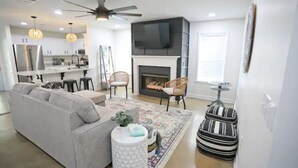 Ein modernes Wohnzimmer mit Sofa, Sesseln, Kamin und einer Küche im Hintergrund.