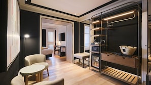 Habitación de hotel pequeña con cama, escritorio, silla, mesita y armario empotrado con estantes.