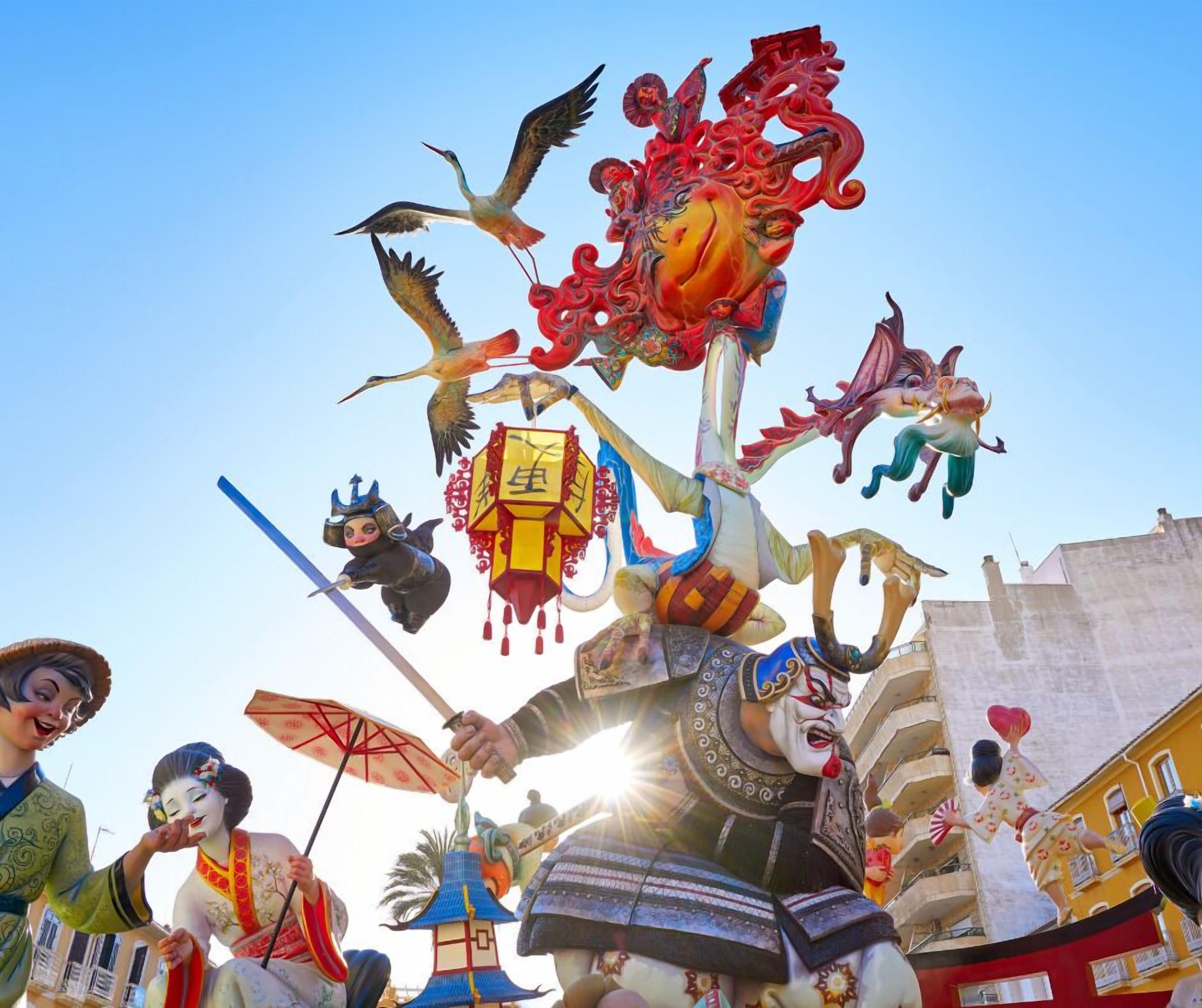 Um festival tradicional com artistas em trajes elaborados, incluindo uma figura com uma grande coroa e outra vestida com um quimono.