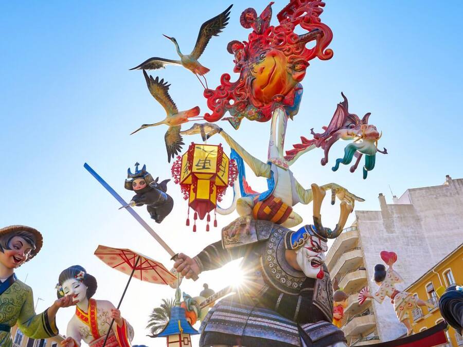 Um festival tradicional com artistas em trajes elaborados, incluindo uma figura com uma grande coroa e outra vestida com um quimono.