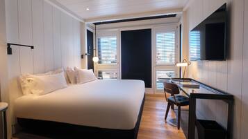 A modern hotel room with a large bed, a desk with a chair, and a TV mounted on the wall.