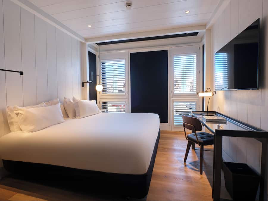 A modern hotel room with a large bed, a desk with a chair, and a TV mounted on the wall.