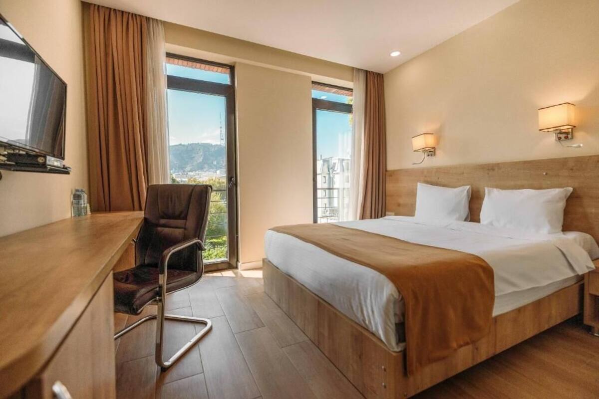 A hotel room with a bed, a desk, a chair, and a view of the outdoors.