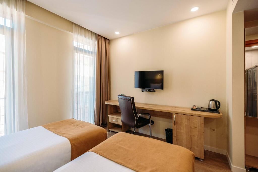 A hotel room with two beds, a desk with a chair, a television, and a wardrobe.