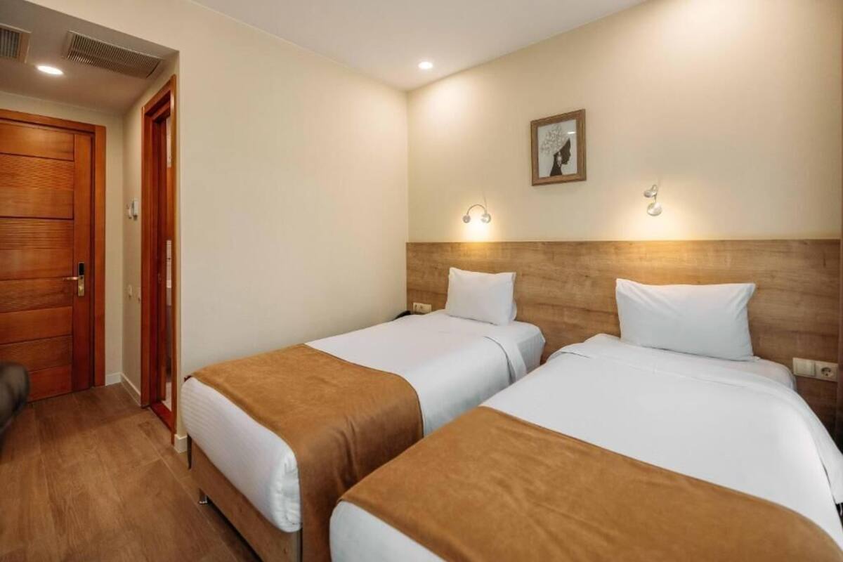 A hotel room with two single beds, wooden headboards, a wooden door, and a small framed picture on the wall.
