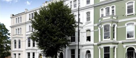 A row of Victorian-style townhouses with white and green facades, black iron railings, and a tree in the foreground.