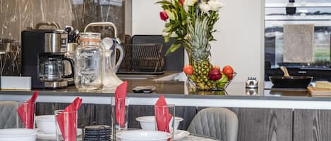 A modern kitchen with a marble backsplash, a coffee maker, a fruit bowl, and a vase with flowers.