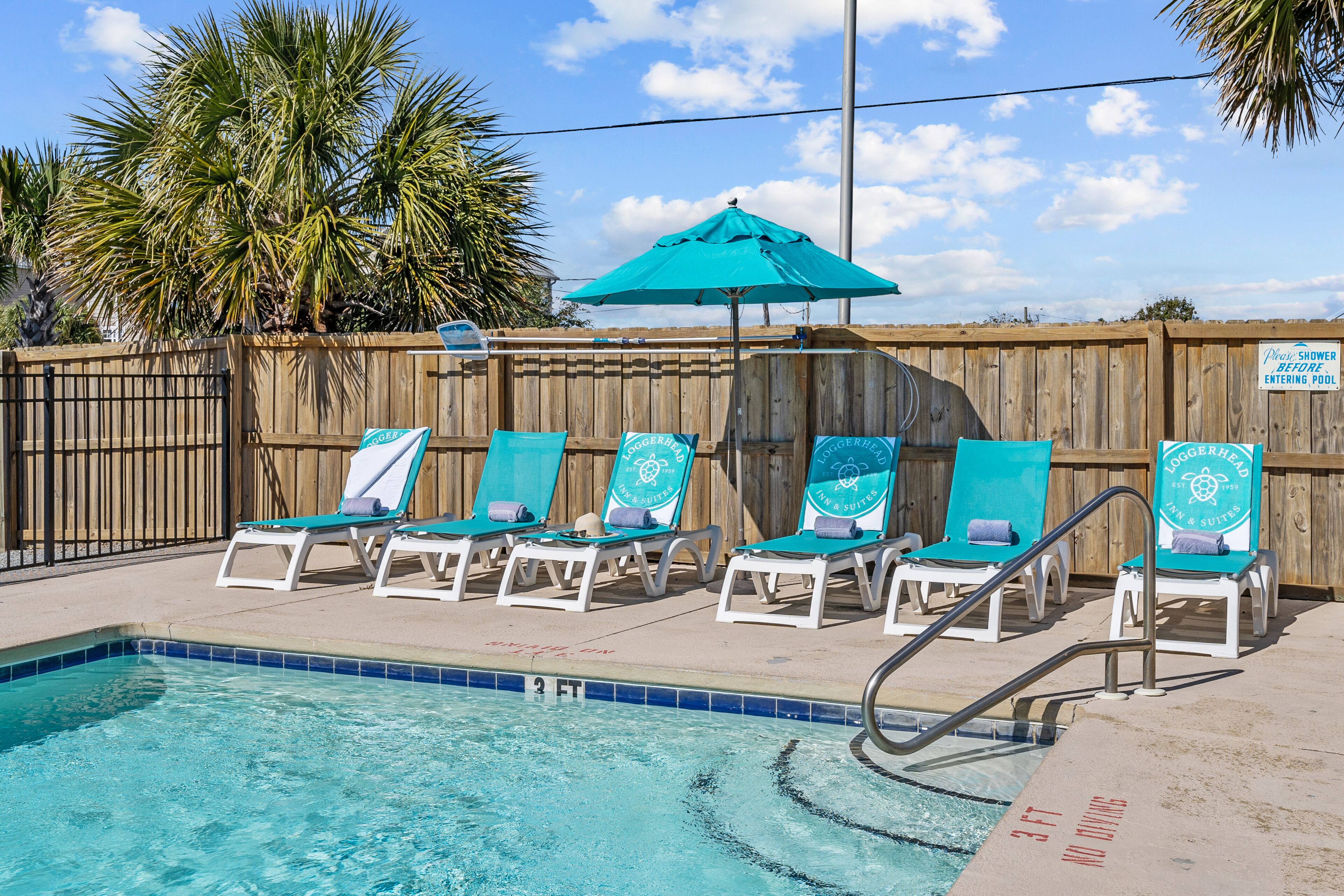 A pool area with lounge chairs and a sign indicating a shower before entering the pool.