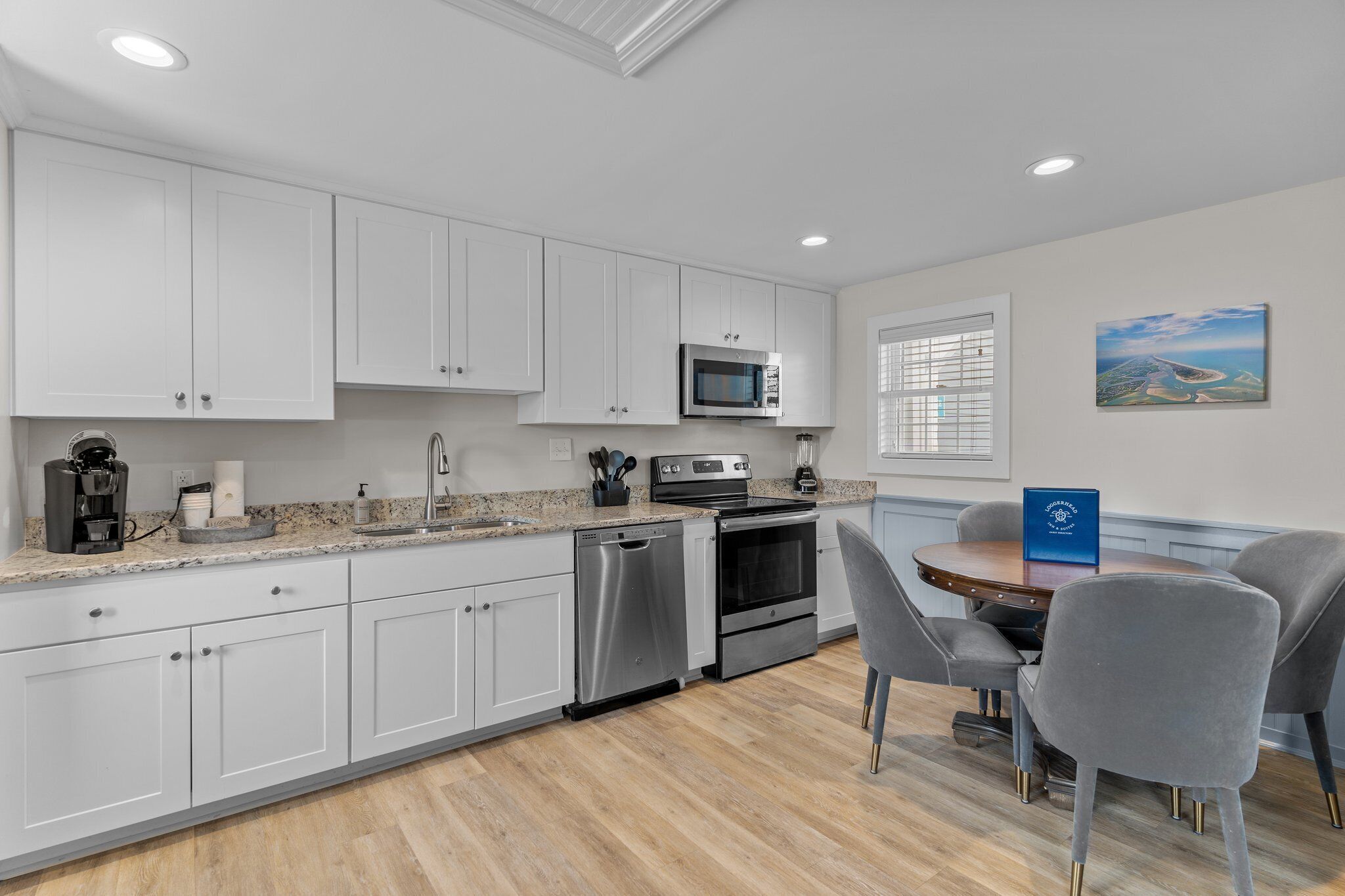 A modern kitchen with white cabinets, stainless steel appliances, a granite countertop, and a dining area with grey chairs.