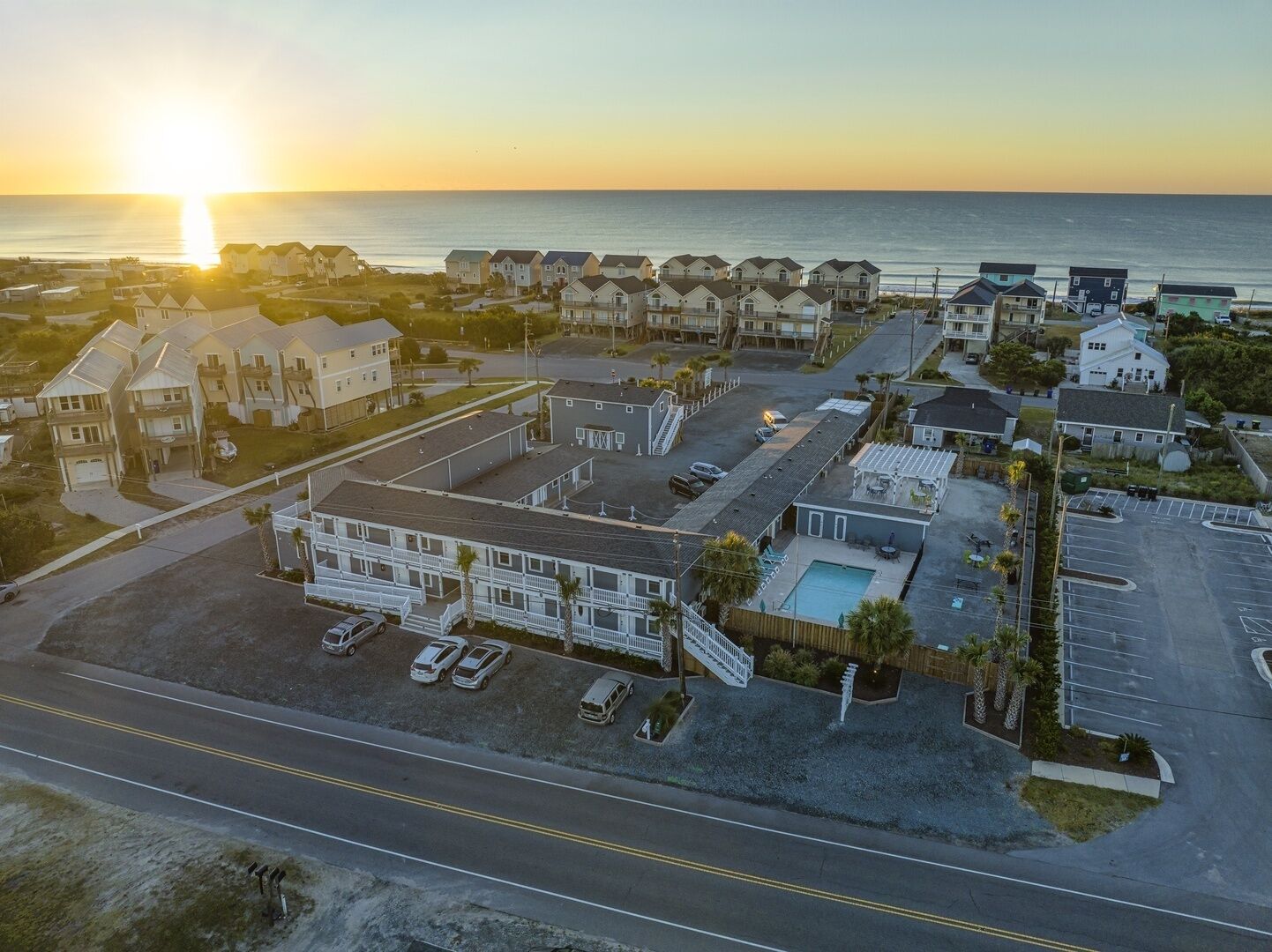 An aerial view of a coastal residential area with houses, a swimming pool, and a parking lot.