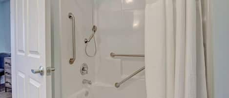 Eine bodenebene Dusche mit Haltegriffen, eine Badewanne und ein weißer Duschvorhang.
