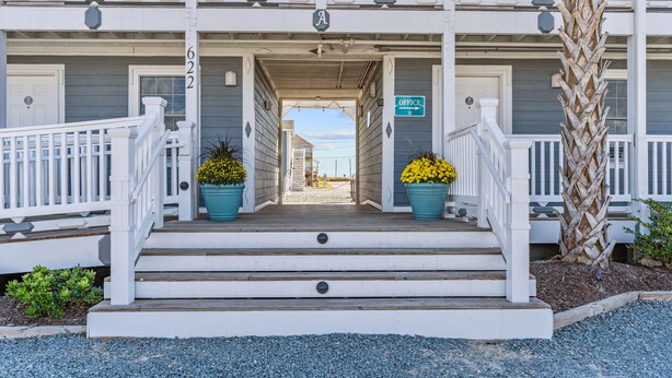 A two-story building with a porch, a sign indicating an office, and a palm tree. - Loggerhead Inn & Suites (Holly Ridge)