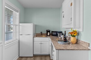 Una cocina compacta con alacenas blancas, un refrigerador, un microondas y un lavamanos.