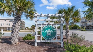 A sign for Loggerhead Inn & Suites with a turtle logo, surrounded by palm trees and a clear sky. - Loggerhead Inn & Suites (Holly Ridge)