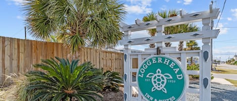 Placa do Loggerhead Inn & Suites, com cerca de madeira e palmeiras ao fundo.