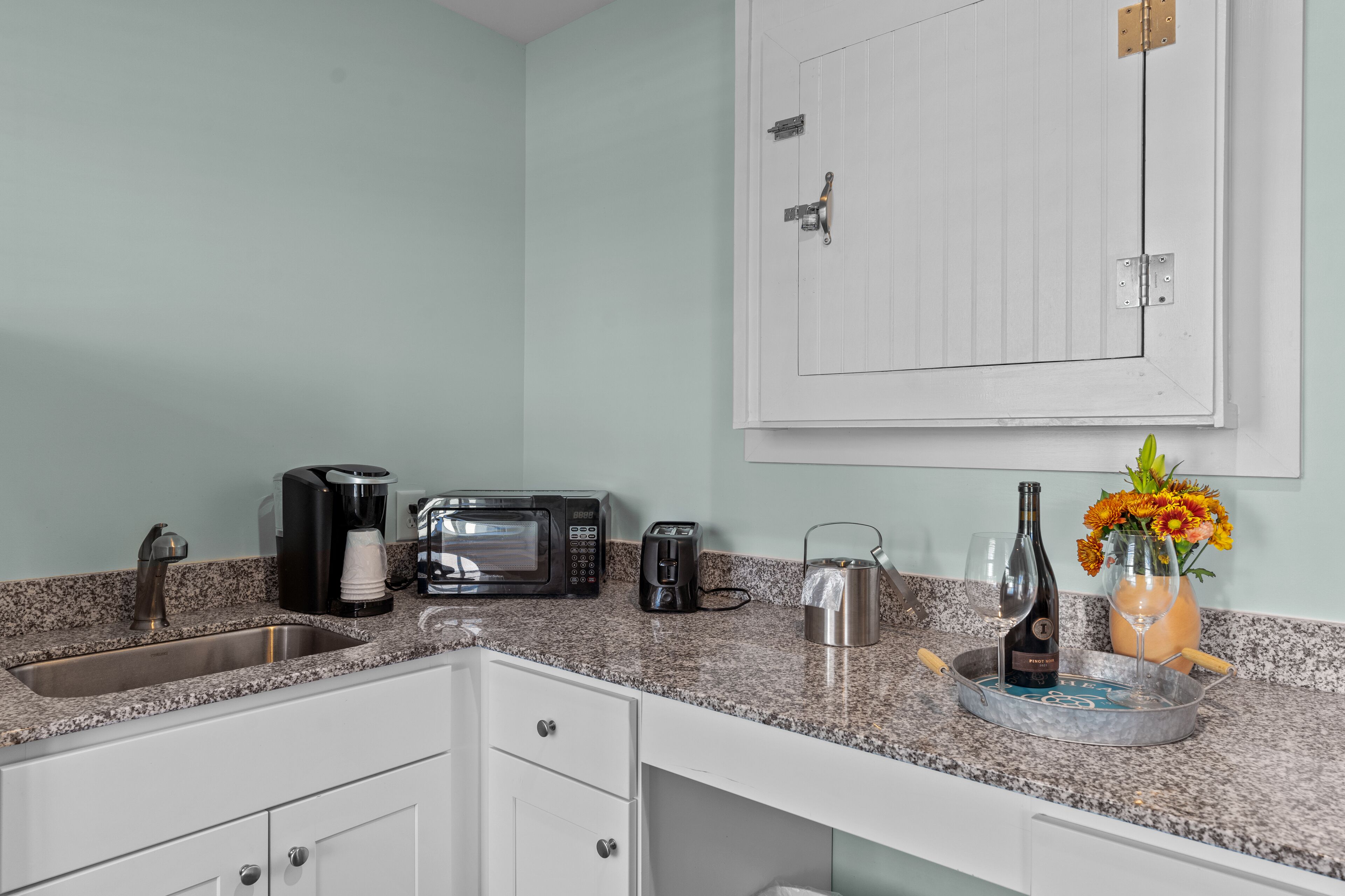 A kitchen with a granite countertop, a coffee maker, a toaster, a kettle, a wine bottle, and a vase with flowers.