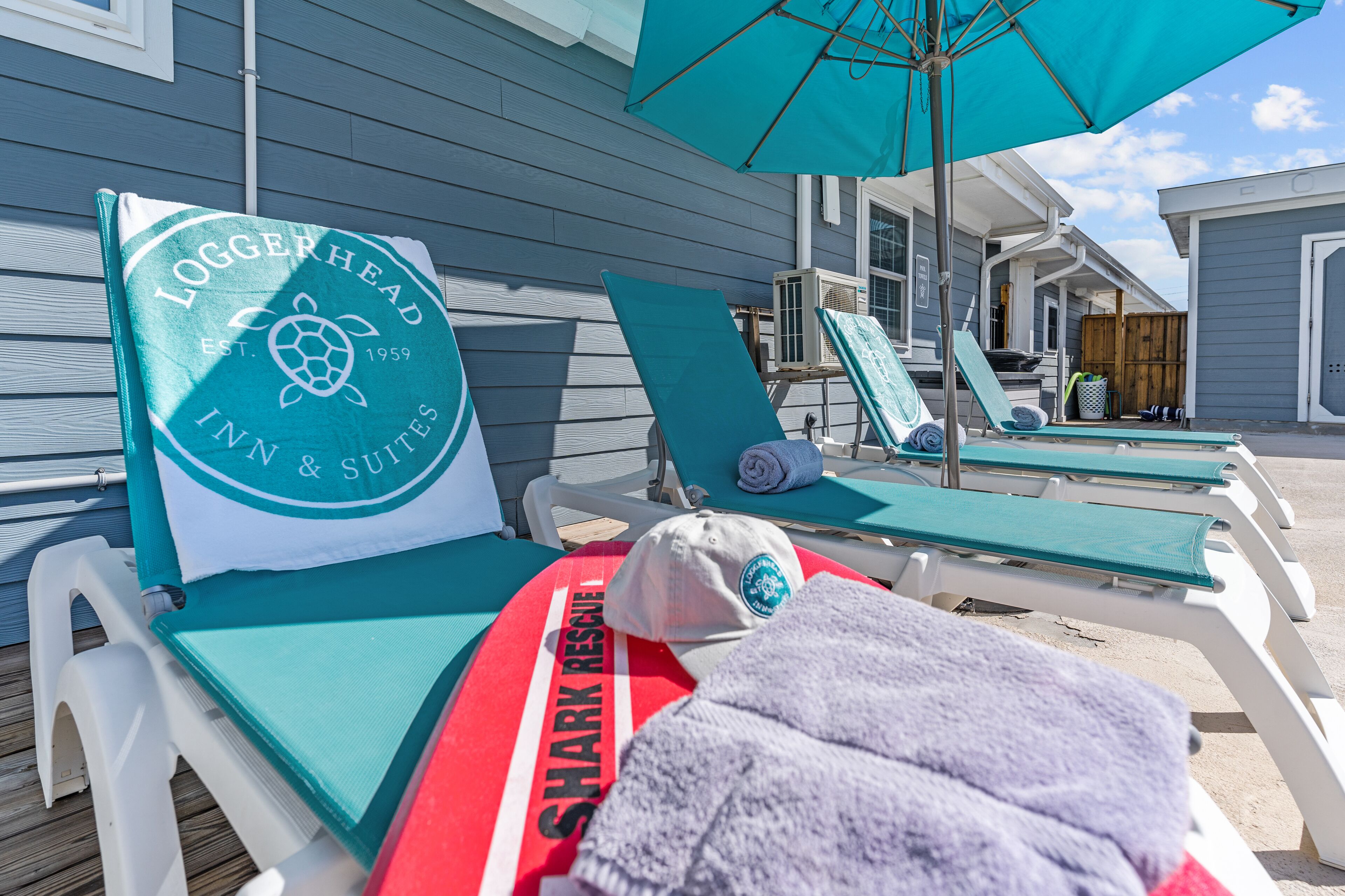 A beachside lounge area with sun loungers, a towel, and a 'Shark Rescue' branded towel.