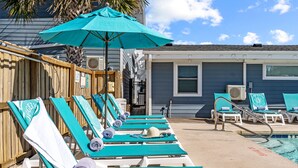 A poolside area with multiple lounge chairs and a large umbrella. - Loggerhead Inn & Suites (Holly Ridge)