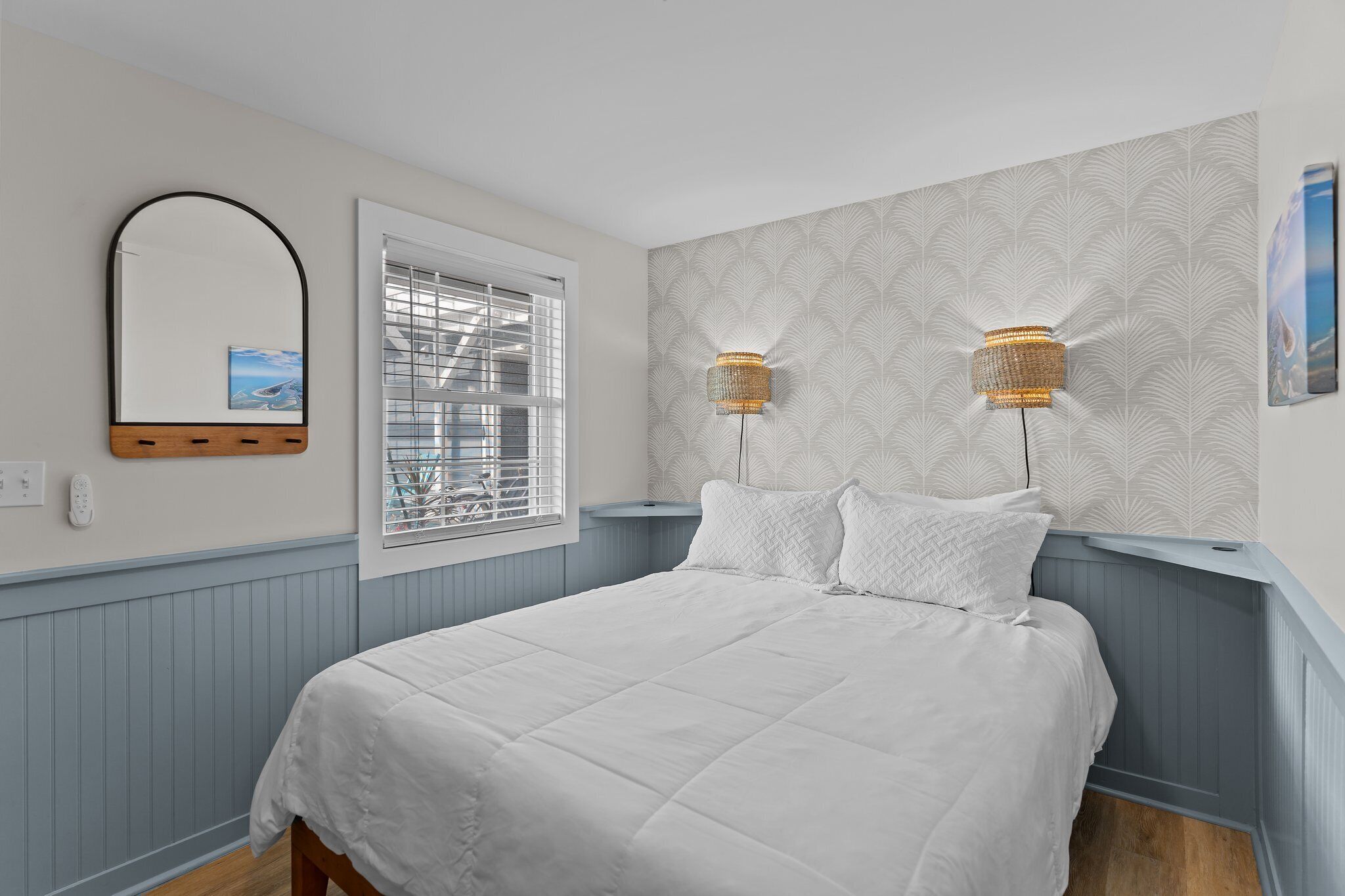 Un dormitorio con cama, una ventana con persianas, un espejo montado en la pared y dos apliques.