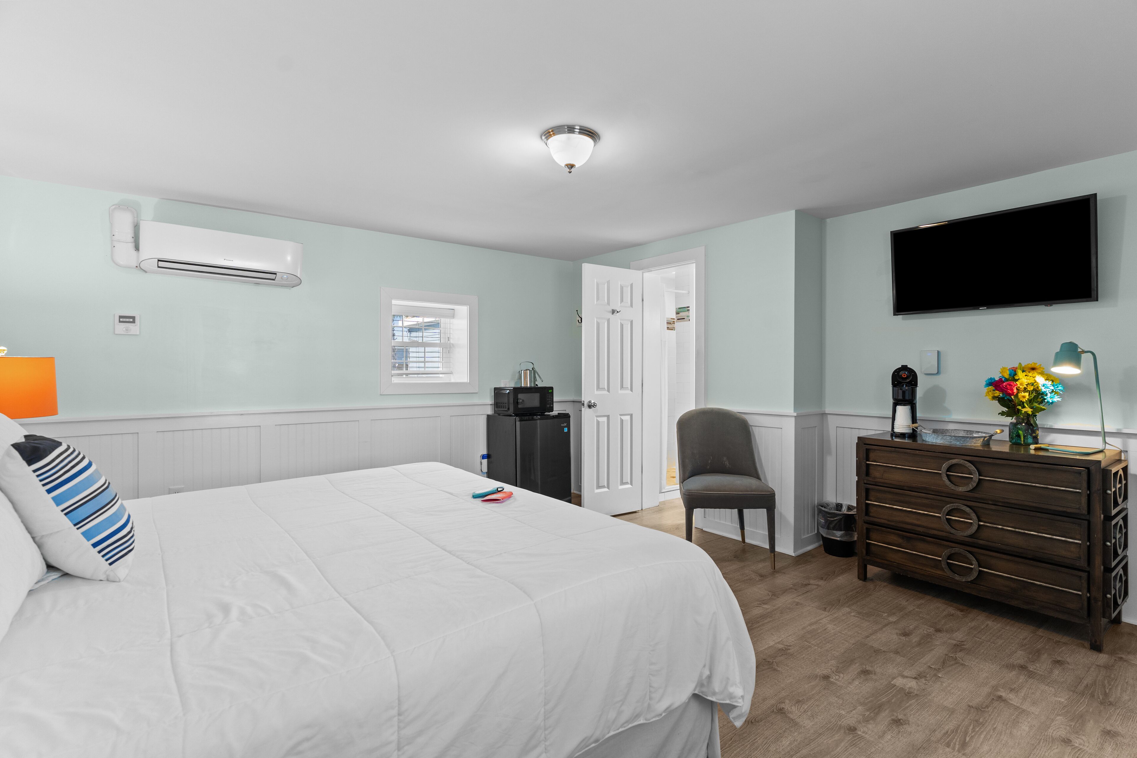 A bedroom with a bed, dresser, TV, and an air conditioning unit.