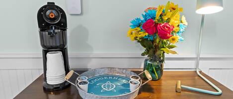 A wooden table with a coffee maker, a tray with a logo, a vase with flowers, and a lamp.