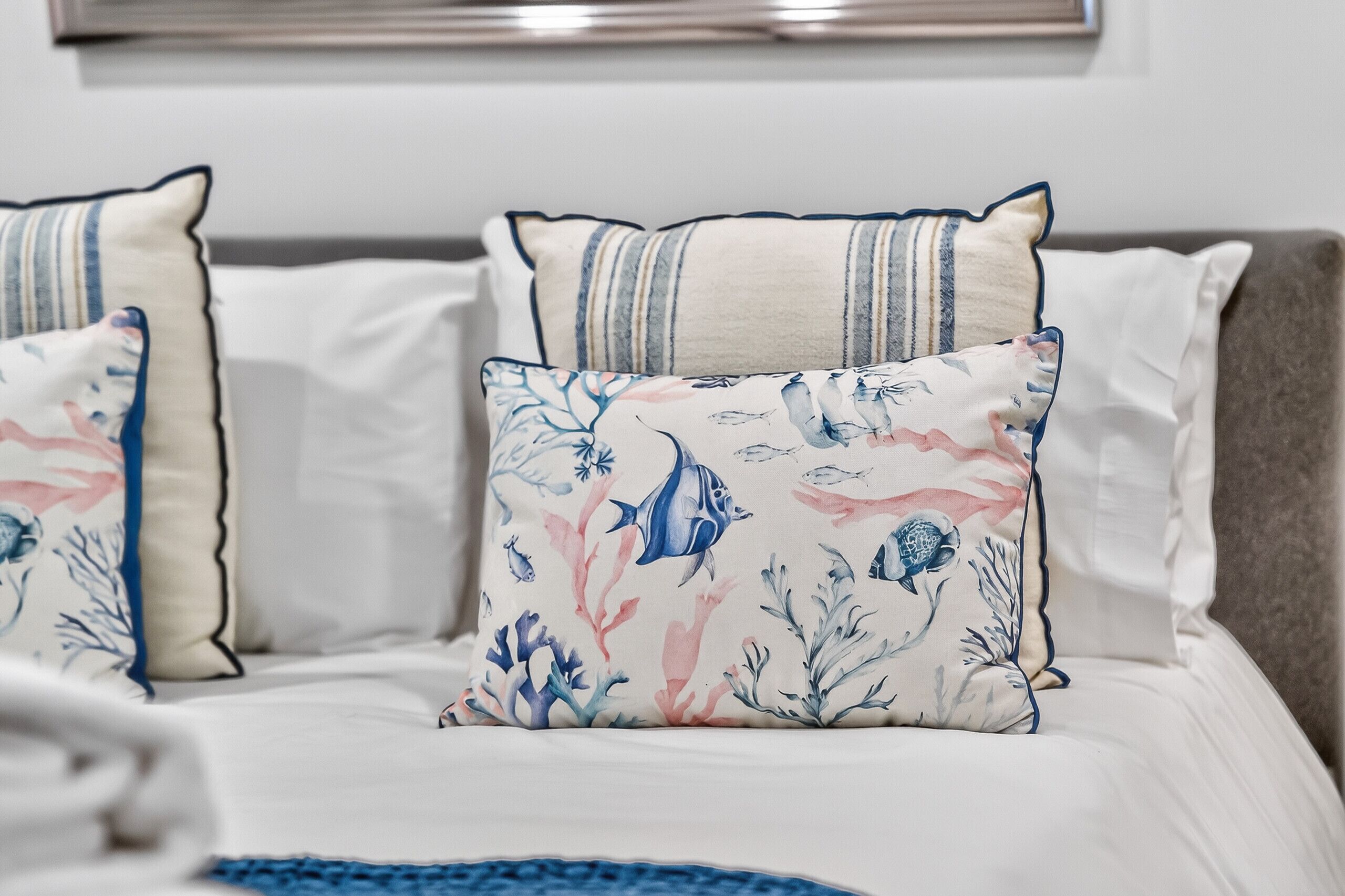 A bed with white bedding, two pillows with a marine-themed design, and a blue throw blanket.