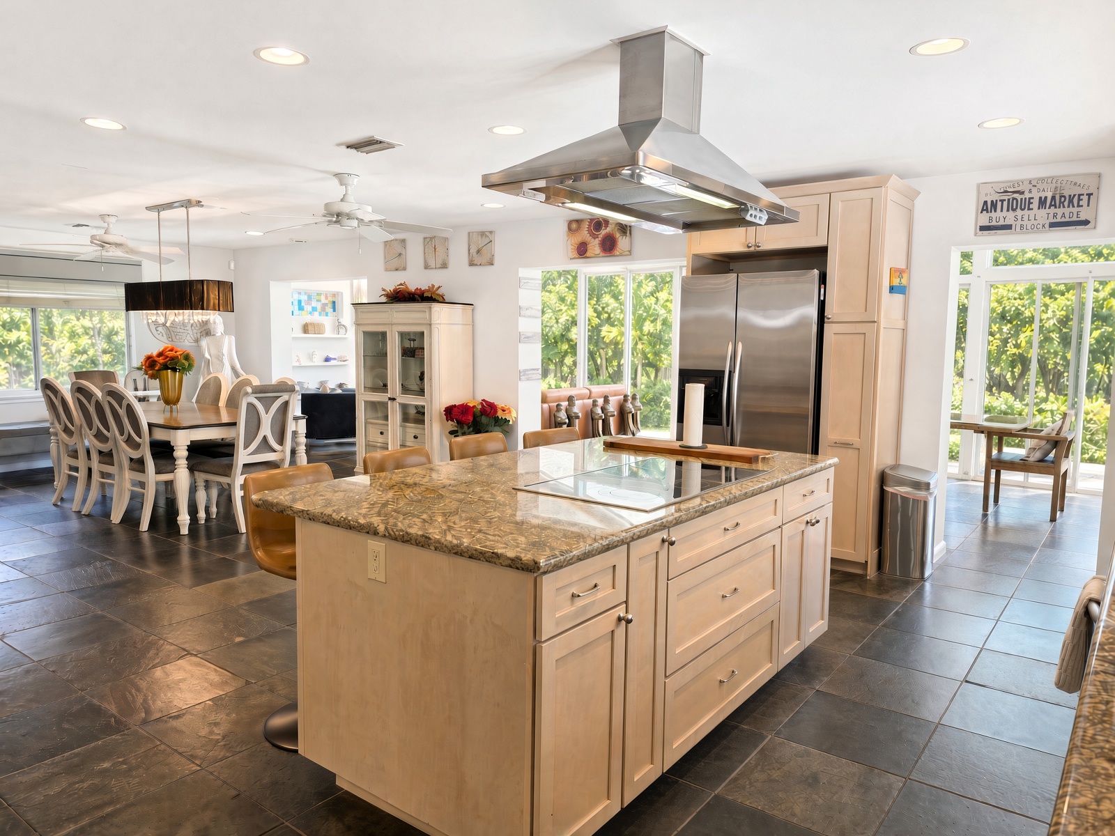 A modern kitchen with a central island, stainless steel appliances, and a view of greenery outside.