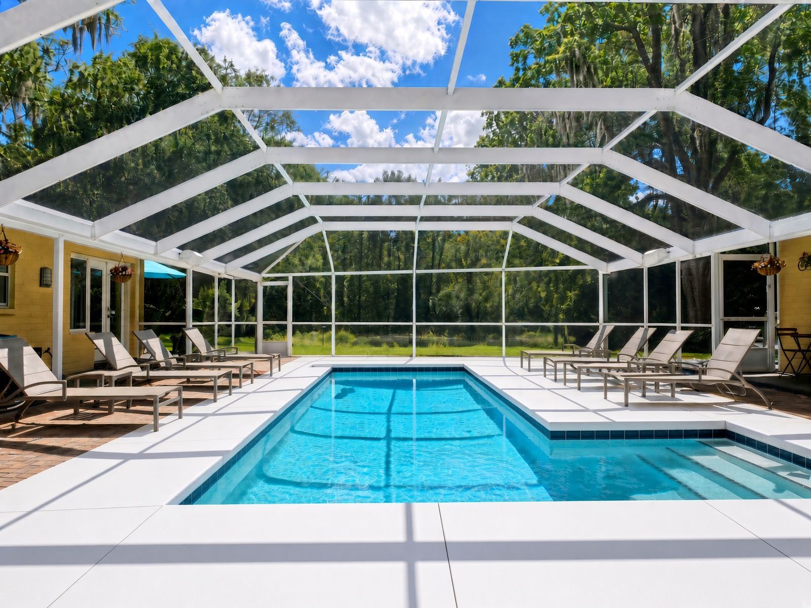 A covered swimming pool with lounge chairs and a view of the surrounding greenery.