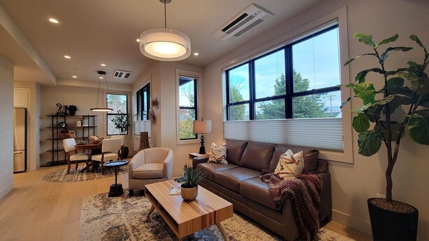 A modern living room with a brown leather sofa, a wooden coffee table, and a large window with blinds.