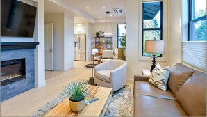 A modern living room with a fireplace, a sofa, a coffee table with a plant, and a dining area in the background.