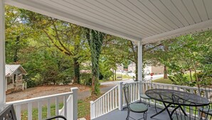 A covered porch with a table and chairs, surrounded by trees and a view of a street. - Downtown Dahlonega Destination - Dog Friendly (Dahlonega)