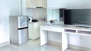 A modern kitchen with a refrigerator, microwave, and stove. There is a dining table with a flat-screen TV and a cabinet above it. - Holiday Hotel 2 (Hai Phong)