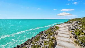 A coastal path leading to a beach with a white umbrella and lounge chairs. - South Bank (Providenciales)