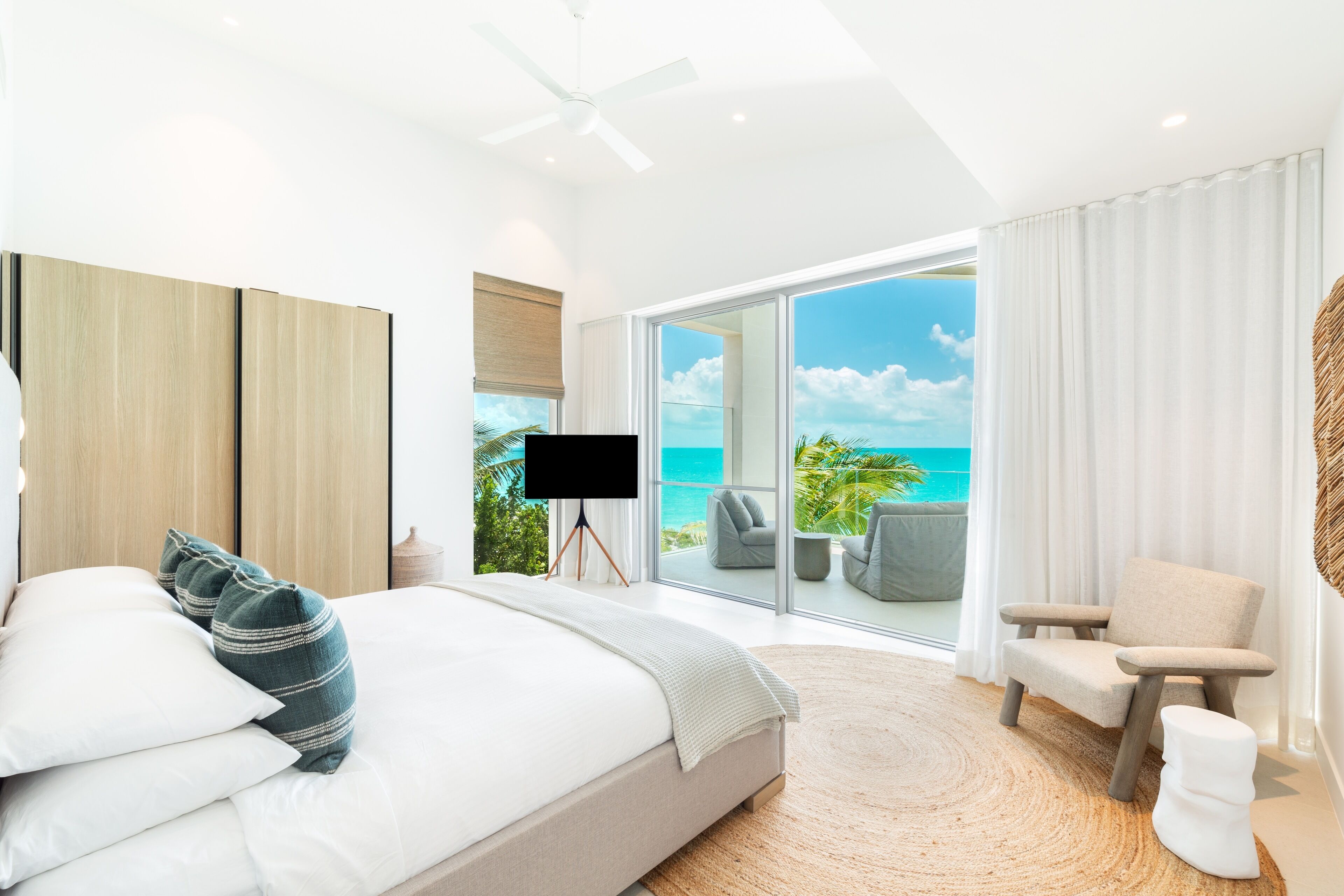 Une chambre moderne avec un grand lit, un téléviseur posé sur un trépied et une vue sur l’océan grâce à de grandes portes vitrées.