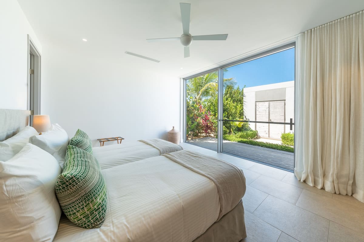 A bedroom with a large bed, a ceiling fan, and a view of a garden through a sliding glass door.