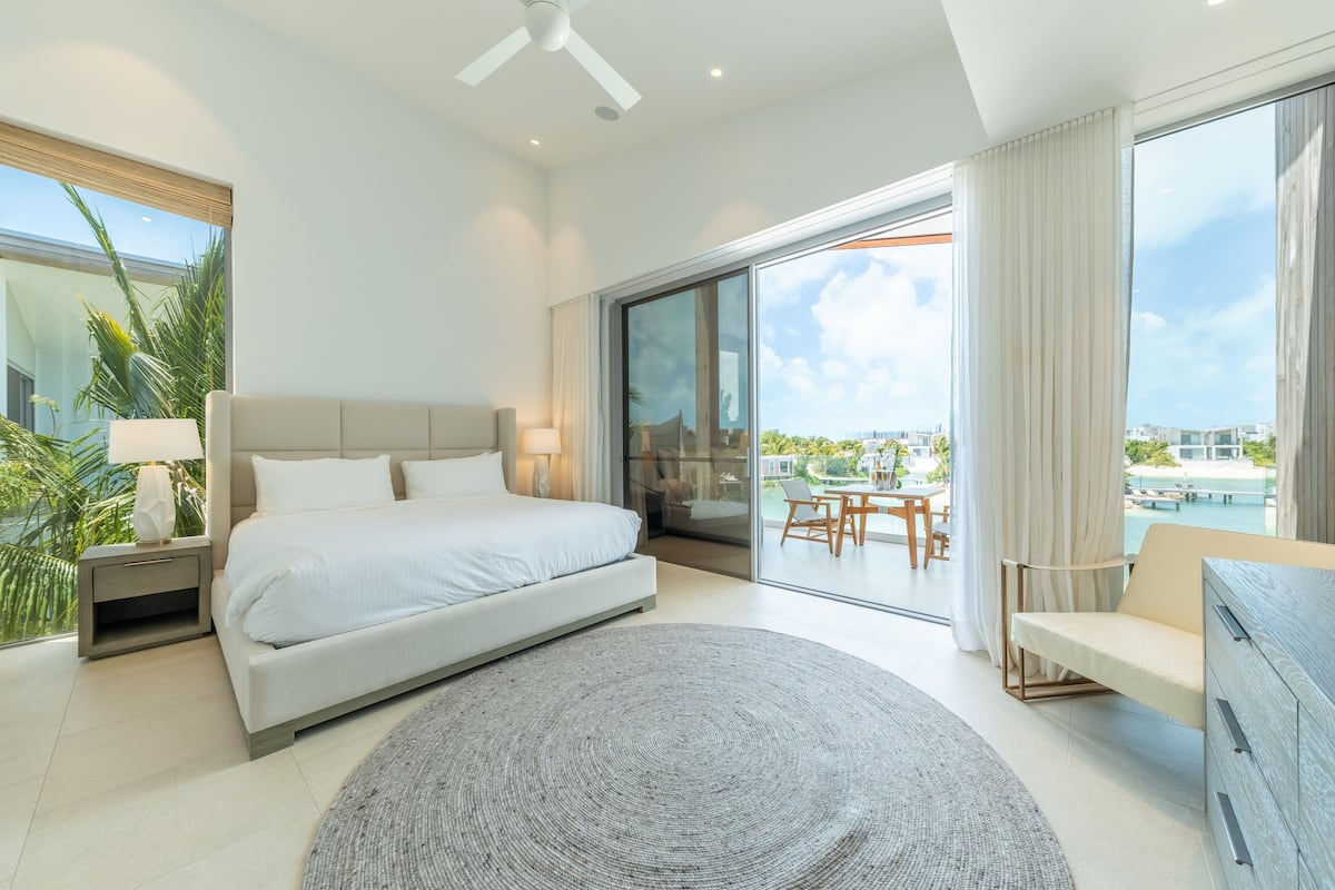 A modern hotel room with a large bed, a desk, and a view of a pool and cityscape.