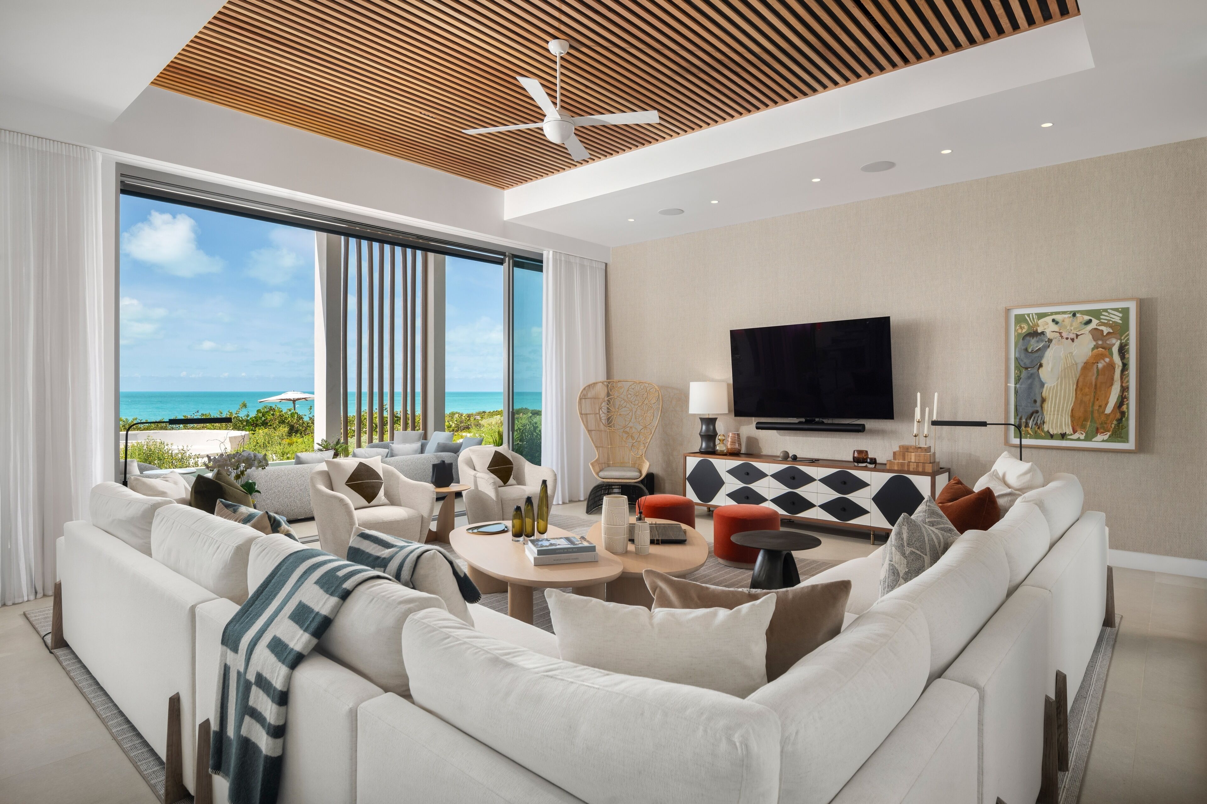 A modern living room with a large window, a ceiling fan, a flat-screen TV, and a view of the ocean.