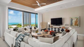A modern living room with a large window, a ceiling fan, a flat-screen TV, and a view of the ocean.