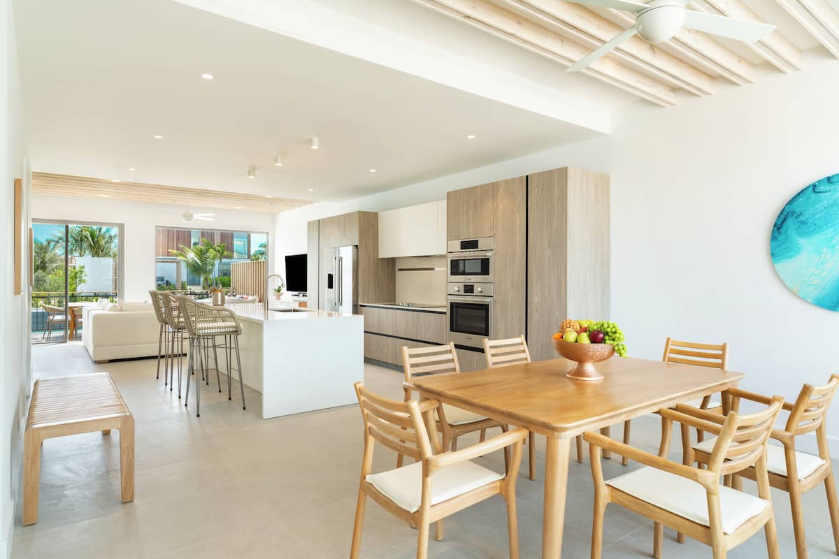 A modern kitchen with wooden cabinets, a central island, and a dining area with wooden chairs and a table.